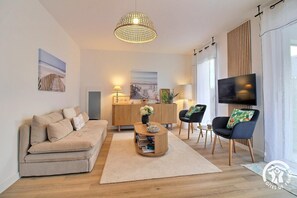 Ein modernes Wohnzimmer mit einer Couch, einem Couchtisch, Stühlen, einem Fernseher und einer Holzkommode mit Kunstwerken.