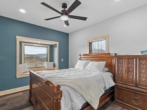 A bedroom with a bed, a ceiling fan, a window with a view, and a wooden wardrobe. - Mountain Reflections | Mtn View+Sunsets & Fire Pit (Newland)
