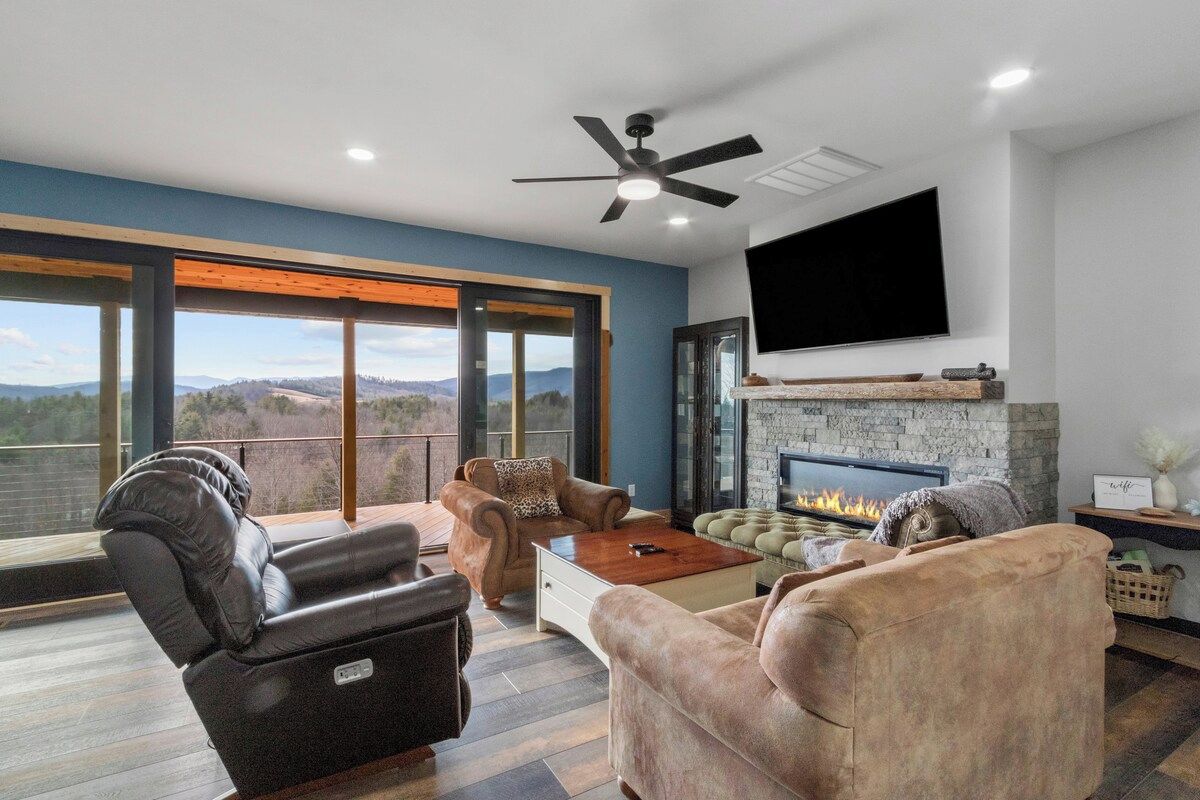 A modern living room with a fireplace, leather sofas, a flat-screen TV, and a balcony with a view.