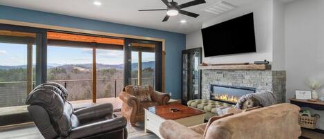 A modern living room with a fireplace, leather sofas, a flat-screen TV, and a balcony with a view.