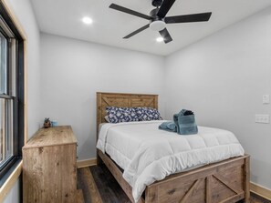 Ein Schlafzimmer mit einem Bettgestell aus Holz, weißer Bettwäsche, einem Deckenventilator und einer kleinen Holzkommode.