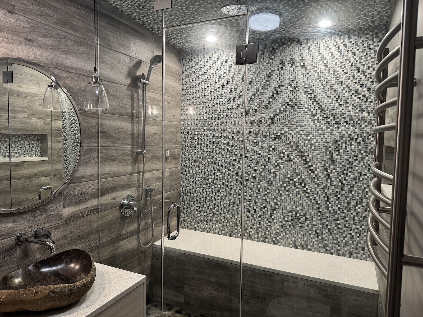 A modern bathroom with a glass-enclosed shower, a round mirror, and a stone sink.