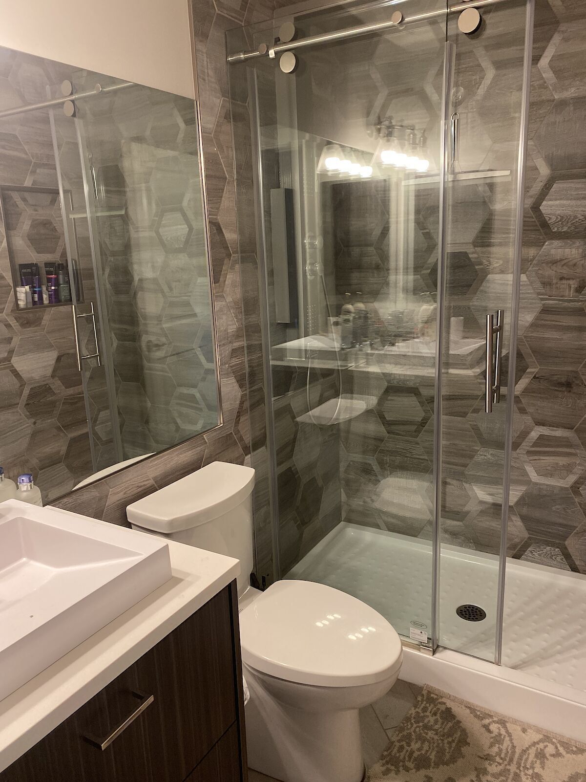 A modern bathroom with a glass shower enclosure, a white toilet, and a vanity with a mirror.