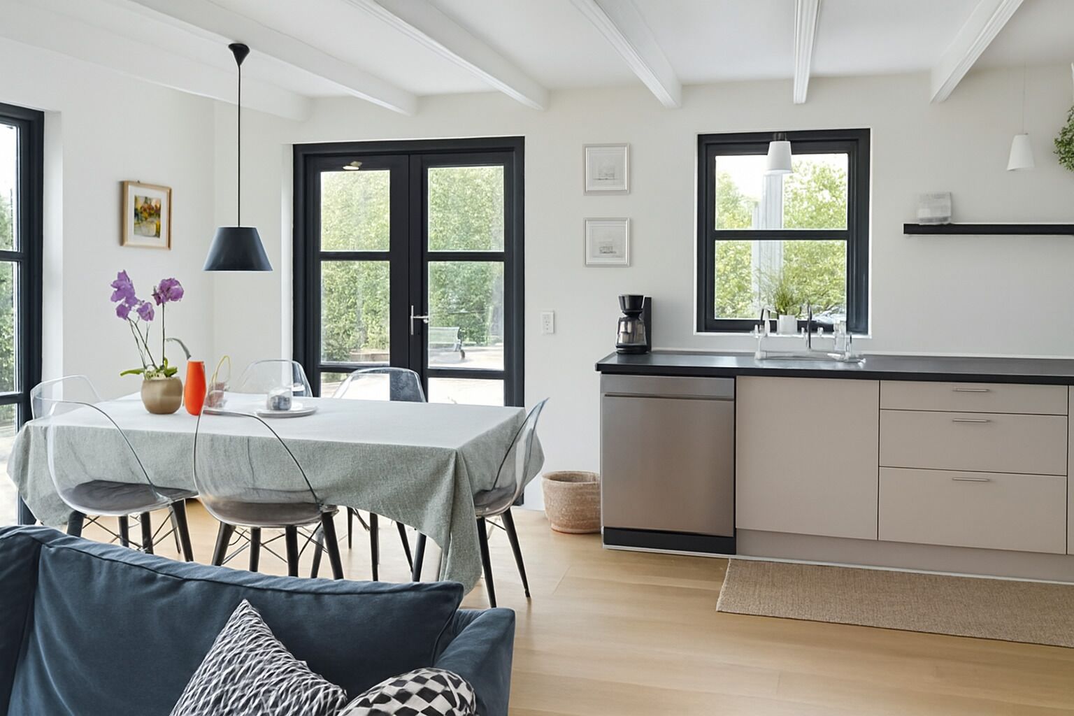 Une cuisine moderne avec un coin repas, comprenant une table dressée pour deux personnes, une machine à café et une vue dégagée grâce à de grandes fenêtres.