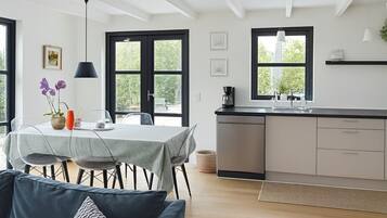 Une cuisine moderne avec un coin repas, comprenant une table dressée pour deux personnes, une machine à café et une vue dégagée grâce à de grandes fenêtres.