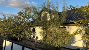 A residential building with a tiled roof, surrounded by trees and a patio area with outdoor furniture. - Lovely holiday home near beach with sauna (Otterup)