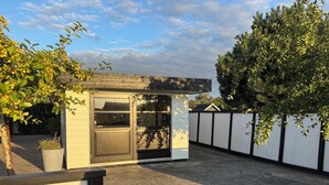 A compact outdoor area with a small structure, possibly a shed, adjacent to a white wall with a black trim. - Lovely holiday home near beach with sauna (Otterup)