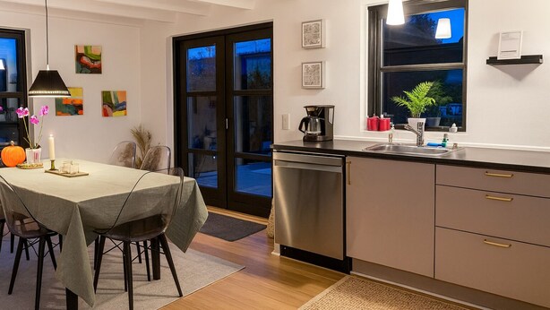 A modern kitchen with a dishwasher, a dining area with a table and chairs, and a view through the glass doors. - Lovely holiday home near beach with sauna (Otterup)