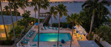 A pool area with lounge chairs and a view of the ocean at dusk.