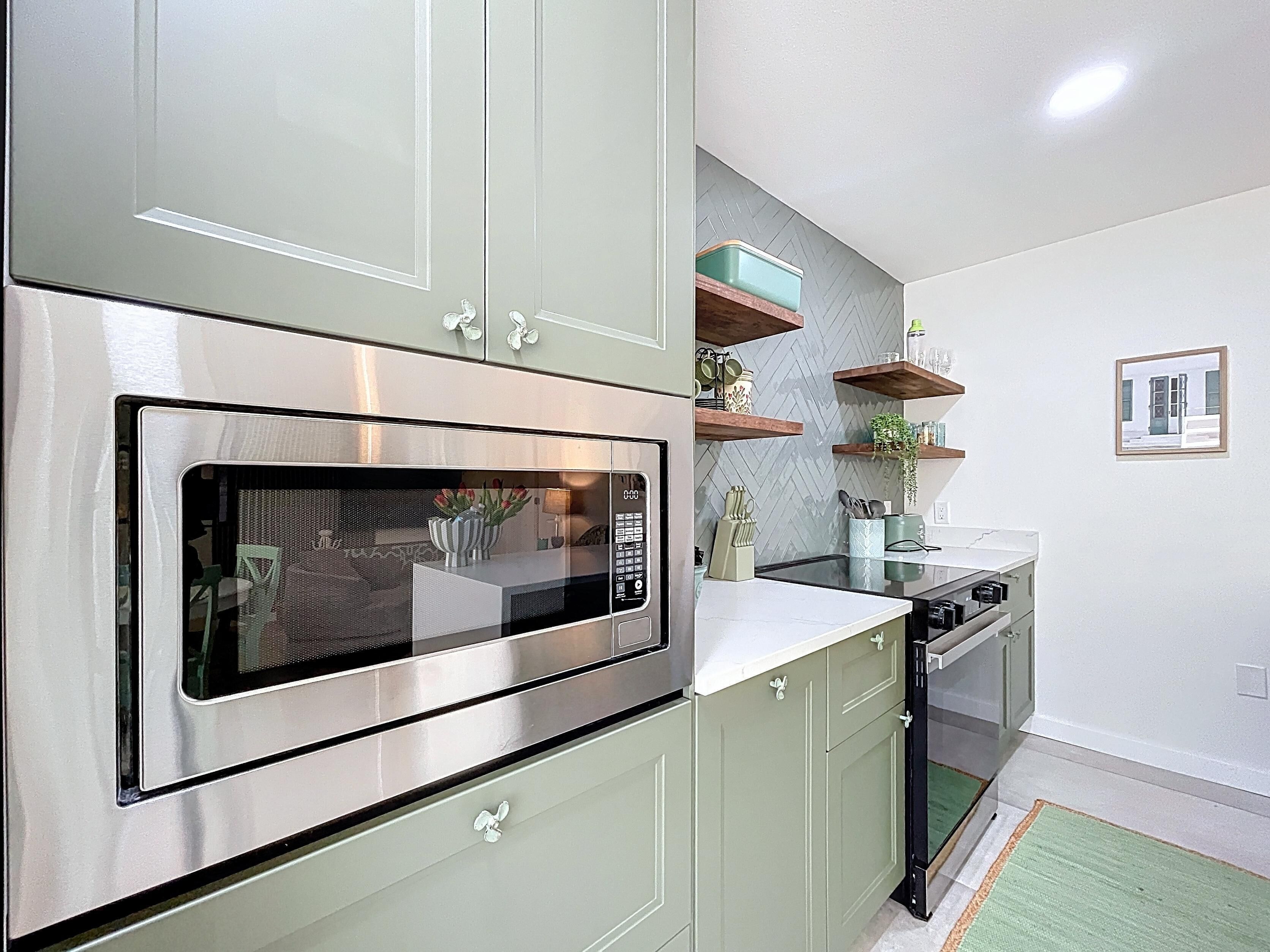 Una cocina moderna con electrodomésticos de acero inoxidable, gabinetes verdes y un salpicadero con motivo de espiga.