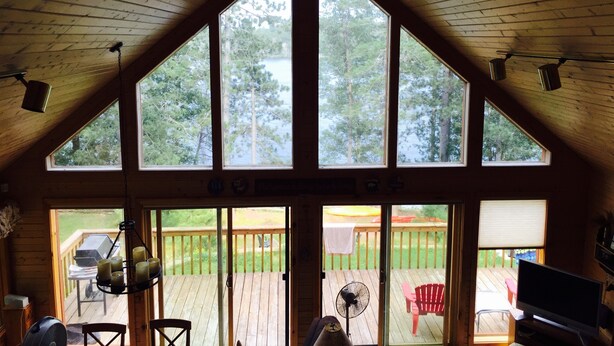 A cabin with a sloped roof, large windows, a ceiling fan, and a view of a deck and outdoor area. - 
Picturesque 4 - Bedroom Lakefront Cabin on the popular Minong Flowage (Minong)