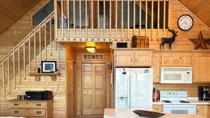 A cozy cabin interior with a wooden staircase, a kitchen with a microwave and refrigerator, a dining area with a bar, and a living room with a leather couch. - 
Picturesque 4 - Bedroom Lakefront Cabin on the popular Minong Flowage (Minong)