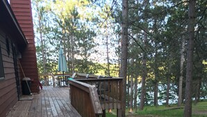 A wooden deck with steps leading to a covered area, surrounded by trees and a dirt path. - 
Picturesque 4 - Bedroom Lakefront Cabin on the popular Minong Flowage (Minong)