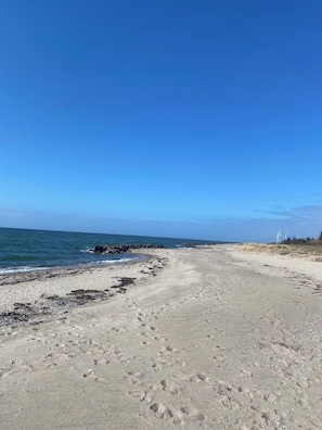 A beach with footprints, a clear sky, and wind turbines in the distance.