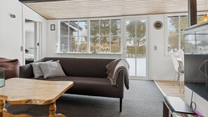 Uma sala de estar moderna com sofá, mesa de centro, televisão e grandes janelas.