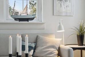 A cozy living room with a sofa, a window with a sailboat model, a lamp, and a framed picture on the wall. - Bright and spacious holidayhome near Vejby Strand (Vejby)