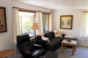 Un salon comprenant un canapé, deux fauteuils, une petite table, une lampe et un tableau accroché au mur.
