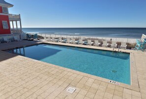 A pool with a view of the ocean, a red building, and lounge chairs. - 6 BR House w Carriage house.Private pool, FREE BIKES,across the street to beach! (Panama City Beach)