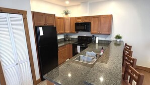 A kitchen with granite countertops, wooden cabinets, a black refrigerator, a microwave, and a sink. - Luxury Condo:  2Bed,1Bath Pool•Hot Tub•Beach•Golf - Canada's warmest lake (Osoyoos)