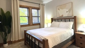 Une chambre à coucher avec un lit, une fenêtre avec des rideaux, une table de chevet, une lampe et une plante.