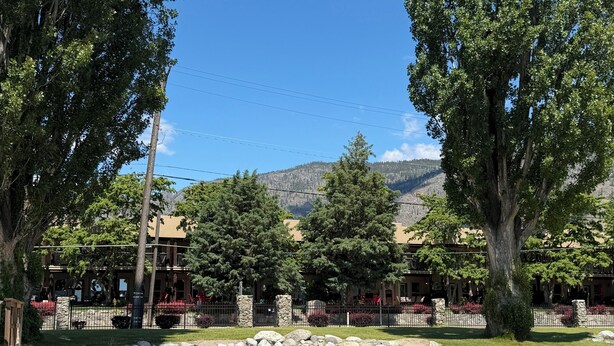 A building with a stone facade, a paved area with a stone wall, and a view of mountains in the background. - Luxury Condo:  2Bed,1Bath Pool•Hot Tub•Beach•Golf - Canada's warmest lake (Osoyoos)
