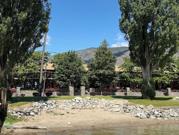 Un bâtiment doté d’une façade en pierre, une zone pavée bordée d’un muret en pierre, et une vue sur les montagnes en arrière-plan.