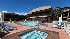 A swimming pool with lounge chairs and umbrellas, surrounded by a fenced area with a building in the background. - Luxury Condo:  2Bed,1Bath Pool•Hot Tub•Beach•Golf - Canada's warmest lake (Osoyoos)