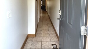 A narrow hallway with a tiled floor, a door on the right, and a light fixture on the ceiling. - Luxury Condo:  2Bed,1Bath Pool•Hot Tub•Beach•Golf - Canada's warmest lake (Osoyoos)