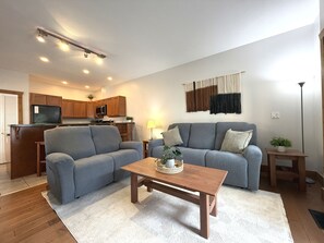 Ein Wohnzimmer mit einer Sofagarnitur, einem Couchtisch und einer Küche im Hintergrund.