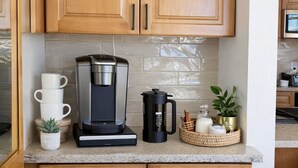 A kitchen with wooden cabinets, a coffee maker, stacked white cups, a potted plant, and a woven basket with kitchen items. - Dillon Lakefront Luxury w Iconic Mountain Views. Walk to Marina & Amphitheater (Dillon)