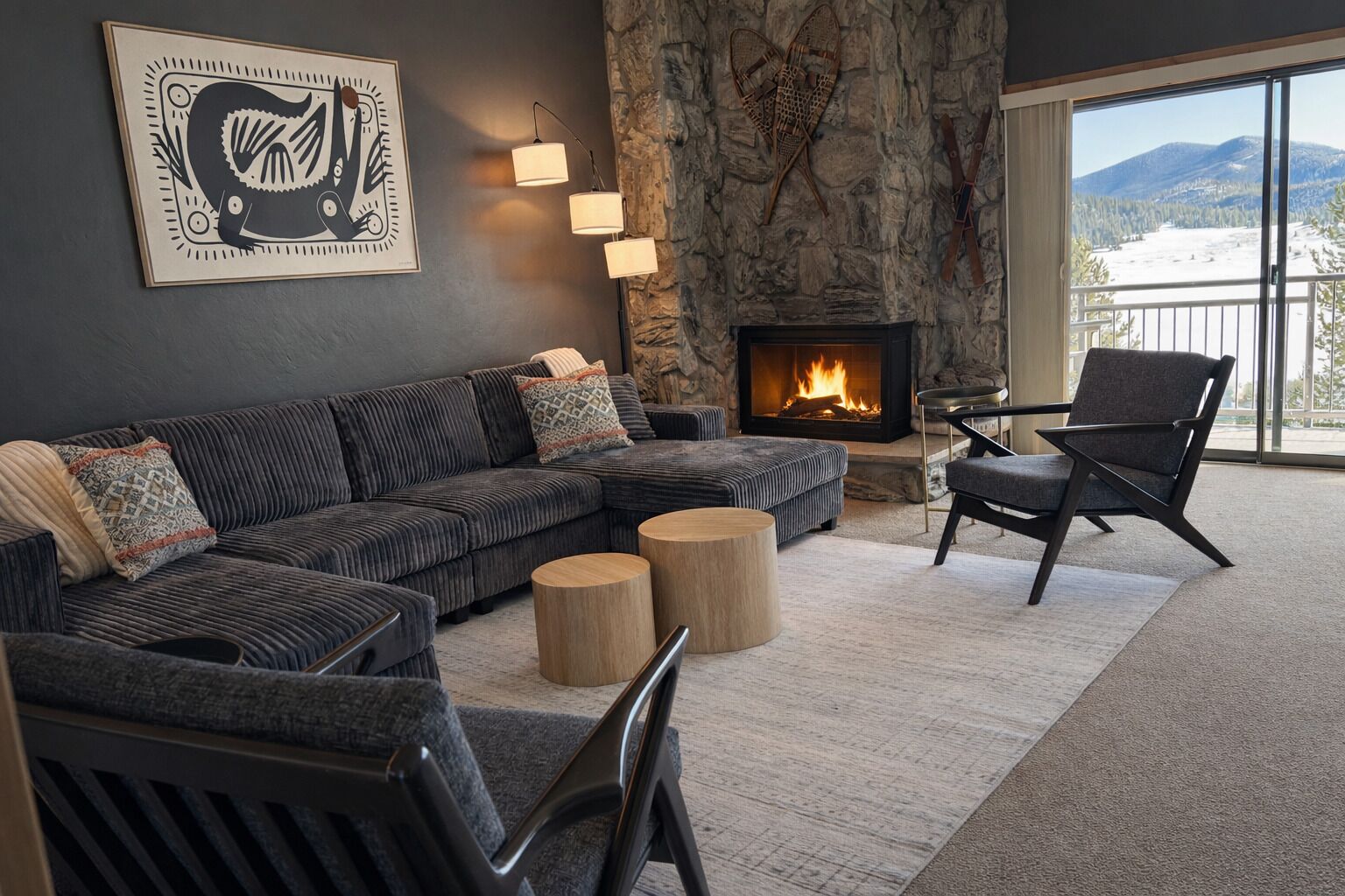 A modern living room with a sectional sofa, a fireplace, a stone accent wall, and a view of the outdoors.