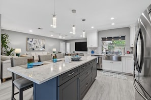 Une cuisine moderne dotée d’un grand îlot central, de meubles blancs, d’appareils électroménagers en acier inoxydable et de luminaires suspendus.
