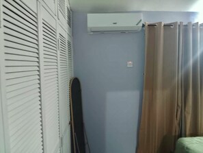 Ein Zimmer mit einem weißen Kleiderschrank, einem braunen Vorhang und einer weißen Klimaanlage an der Wand.