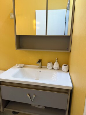 Ein Badezimmer mit einem weißen Waschbecken, einem Spiegel darüber und einer gelben Wand.