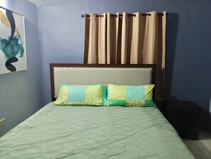 Un dormitori amb un llit, un capçal de llit, una cortina i una paret amb un quadre.