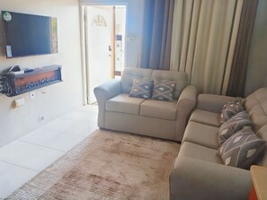 Ein Wohnzimmer mit einer Couch, einem an der Wand befestigten Fernseher und einem Fenster mit Vorhängen.