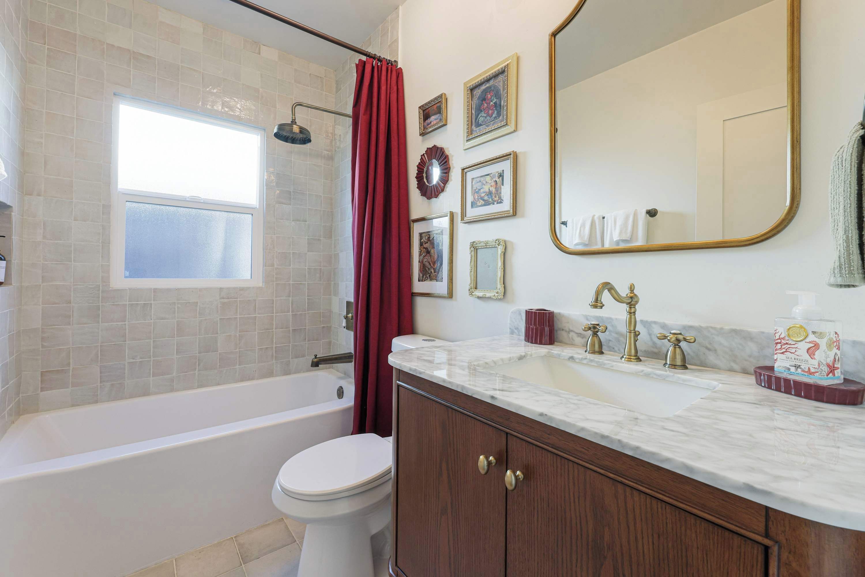 A bathroom with a bathtub, toilet, vanity with a sink, and a large mirror.
