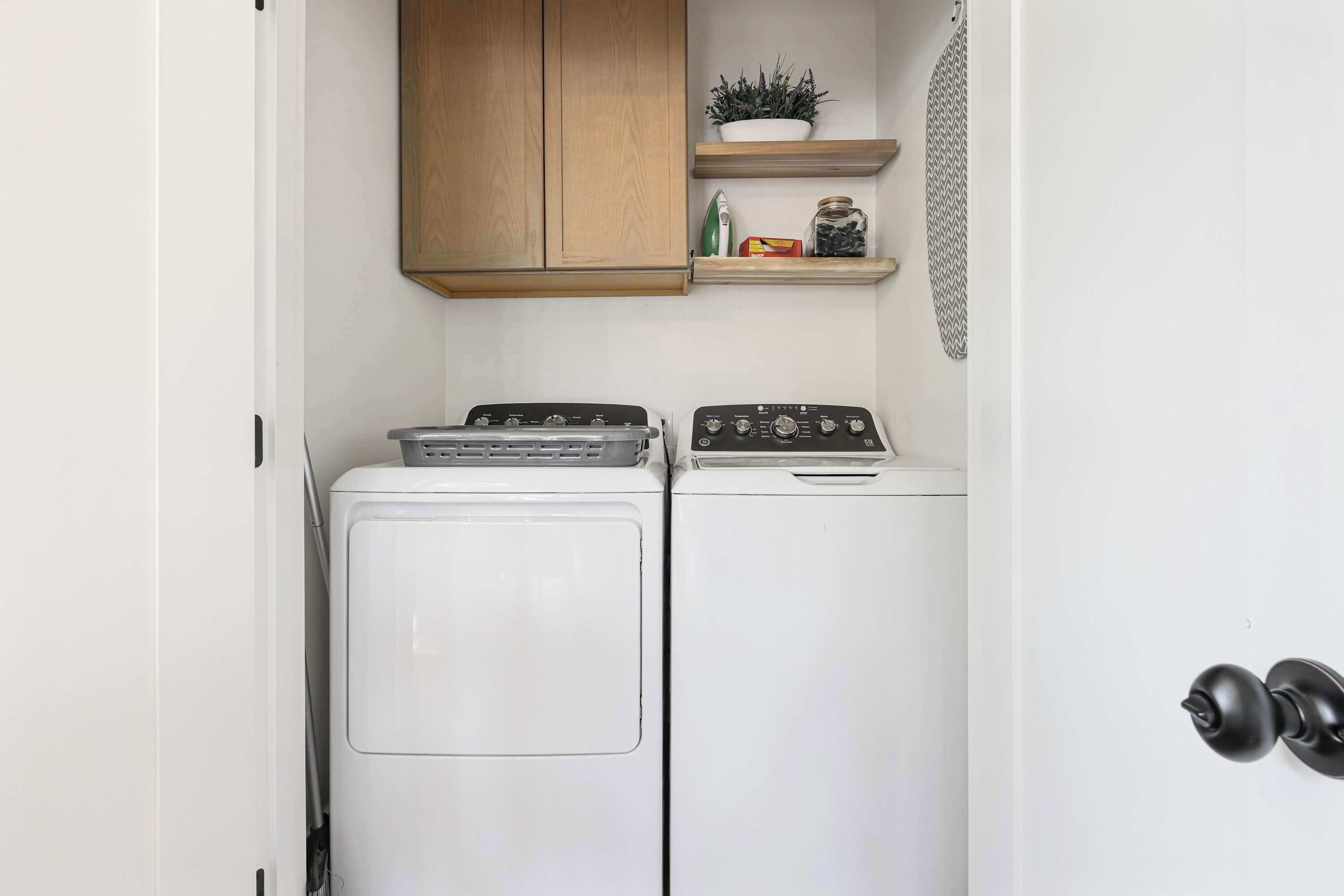 A laundry area with two washing machines, wooden cabinets, and a shelf with decorative items.
