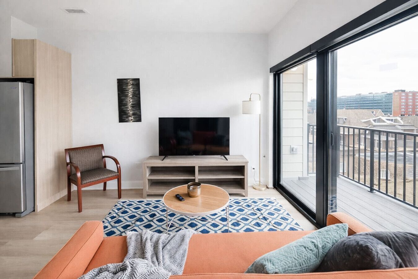 Un salon moderne avec un canapé, un téléviseur, une table basse et une vue sur la ville grâce à de grandes fenêtres.