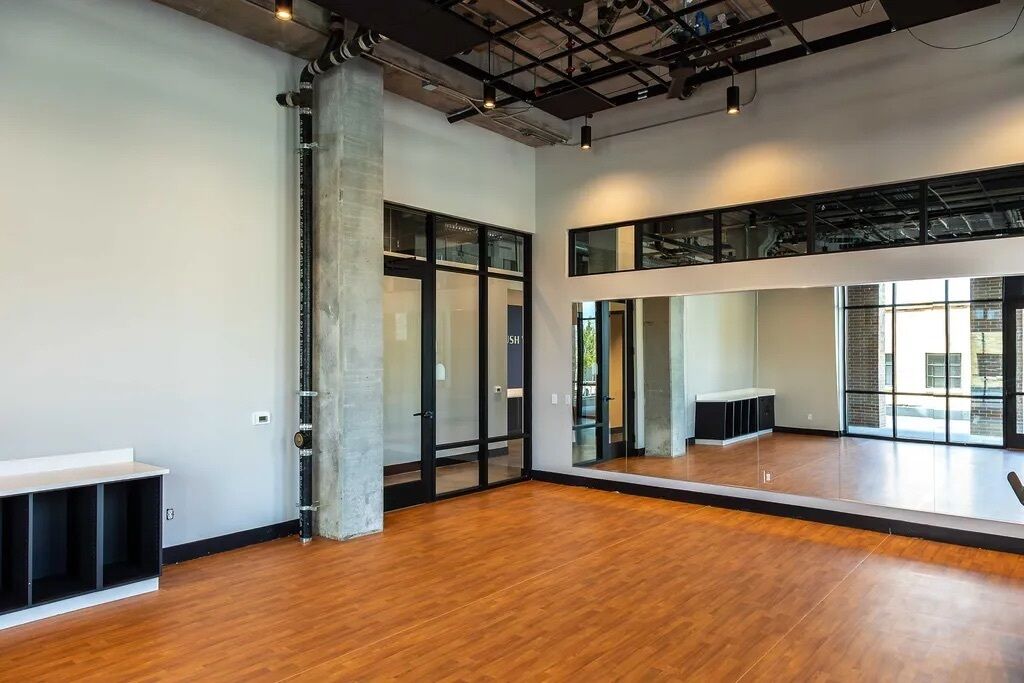 Una habitación amplia con techo alto, conductos expuestos y ventanas grandes.