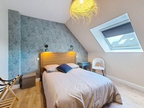 A bedroom with a sloped ceiling, a skylight, a bed with a wooden headboard, a small table, a chair, and a decorative light fixture. - QUIBERON - 2 rooms + - 46m² - city center (QUIBERON)