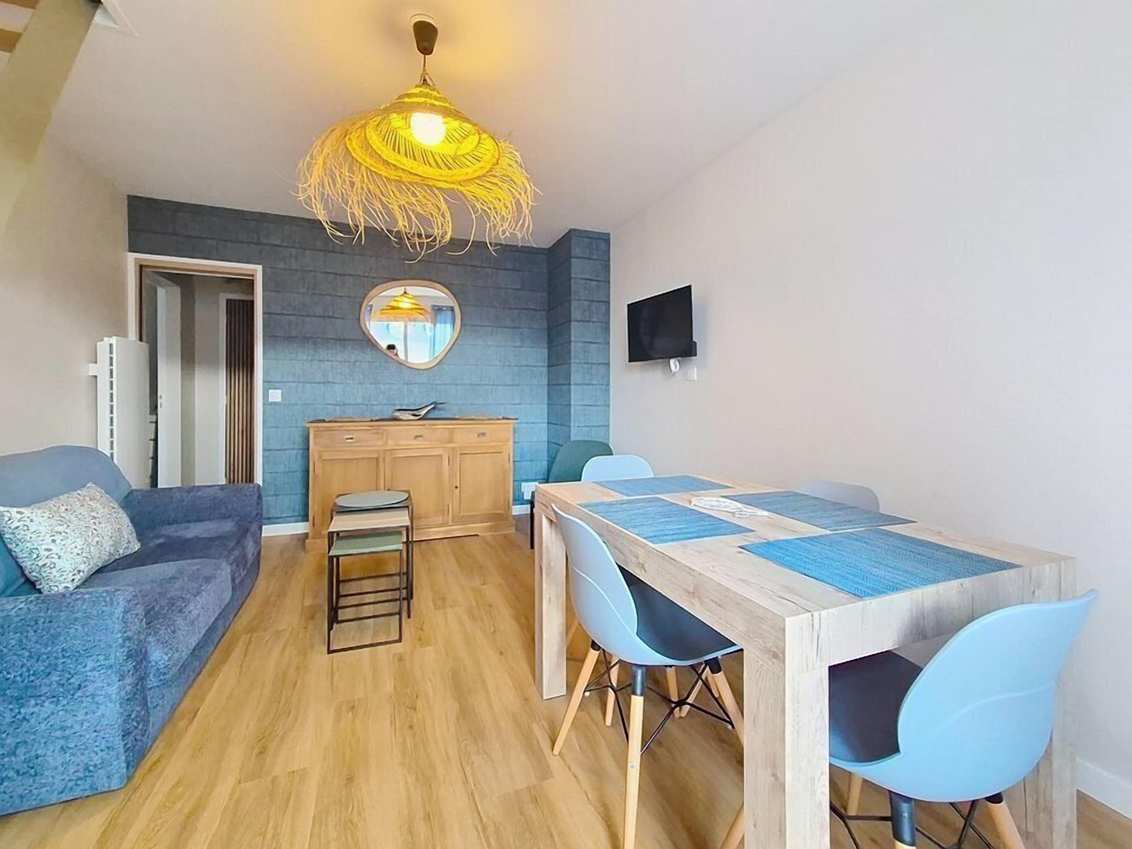 En moderne stue med en sofa, et spisebord med stole, et træskab, et fjernsyn ophængt på væggen og en unik gulvlampe.