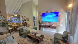 A spacious living room with a large flat-screen TV mounted on the wall, a dining area with a table and chairs, and a cozy seating area with sofas and a coffee table.