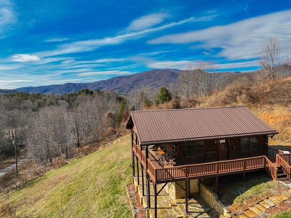 Eine Holzhütte mit einer Holzdiele und einem Steinfundament, umgeben von einer hügeligen Landschaft.