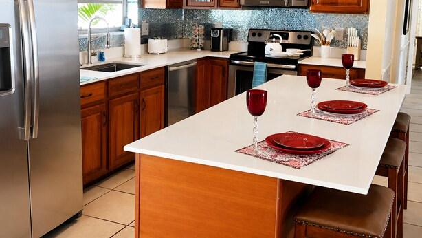 Una cocina con armarios de madera, electrodomésticos de acero inoxidable y una isla central con platos rojos y copas de vino.