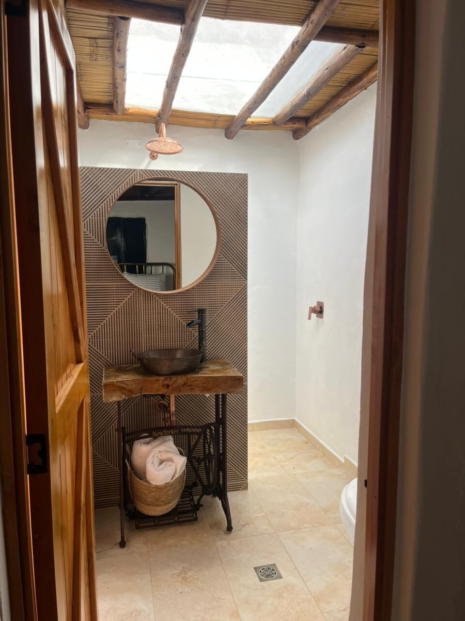 A bathroom with a wooden ceiling, a round mirror, a sink, and a towel rack.