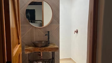 A bathroom with a wooden ceiling, a round mirror, a sink, and a towel rack.