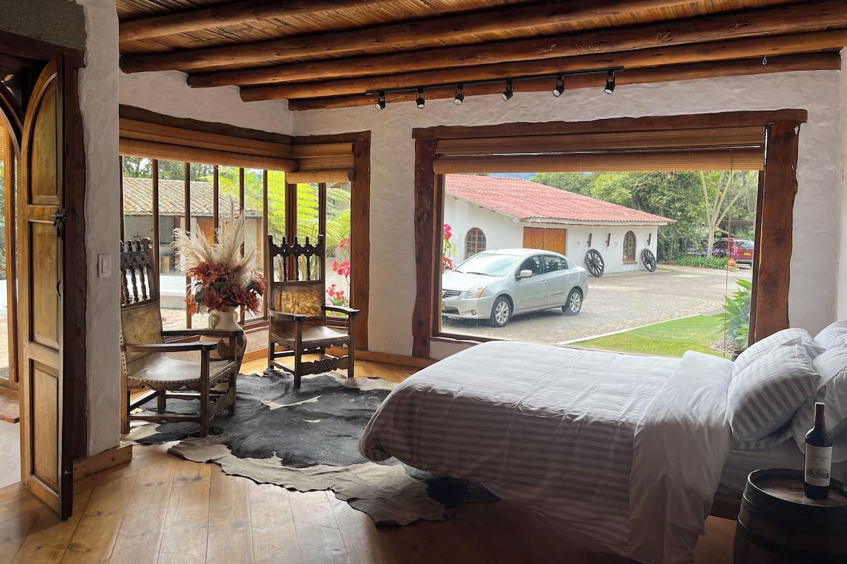 Una habitación con cama, una silla, una mesa y un ventanal grande.