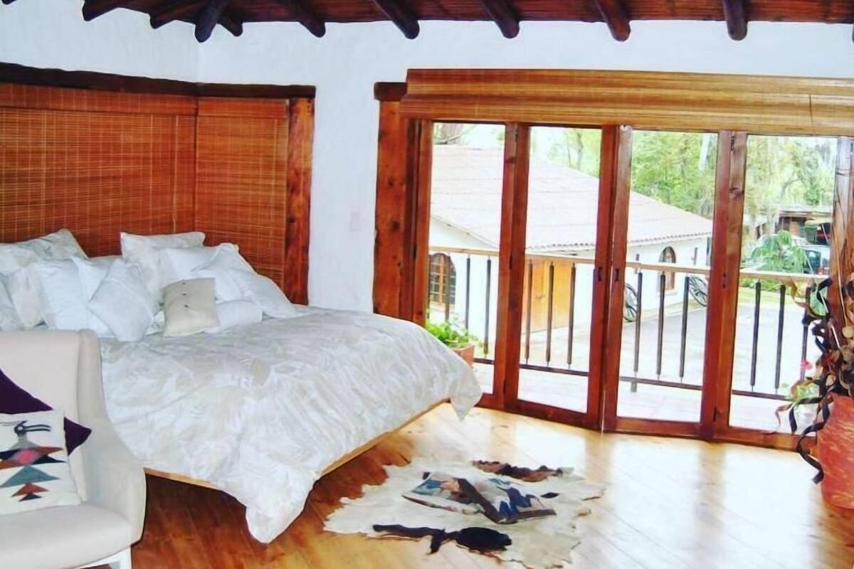Un dormitorio con techo de madera, una cama con ropa de cama blanca, una silla y un ventanal con vistas al exterior.