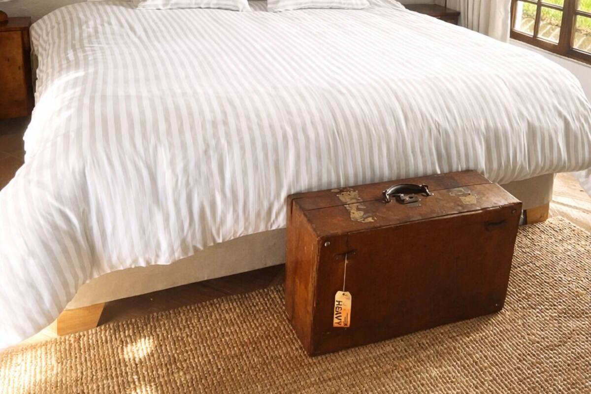 Un dormitorio con una cama grande, un cuadro en la pared, un cofre de madera y una ventana con cortinas.